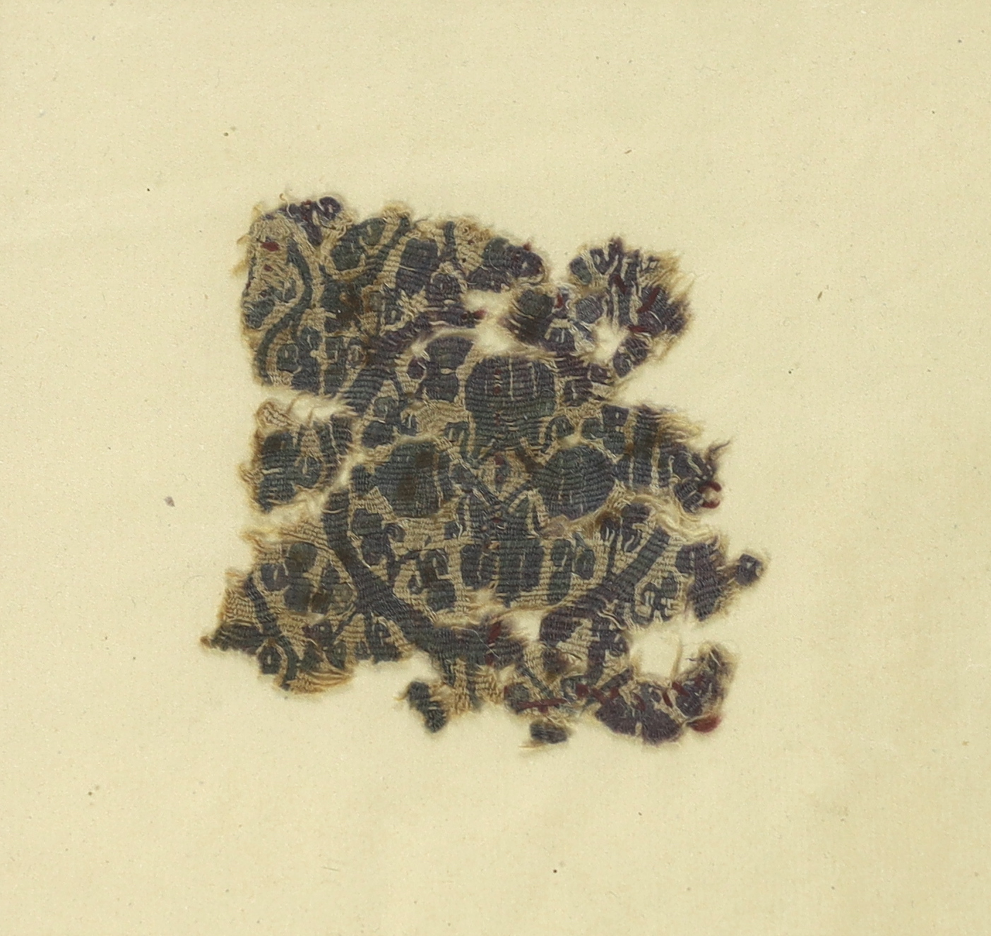 A framed 5th/6th century AD textile - a woven wool fragment, possibly Coptic, with central cartouche of four urns surrounded by vines, worked in blue on an unbleached beige ground (discoloured with age), including typed